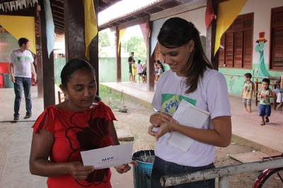 Servidora do MPF entrega fôlder didático sobre as eleições a moradora da comunidade
